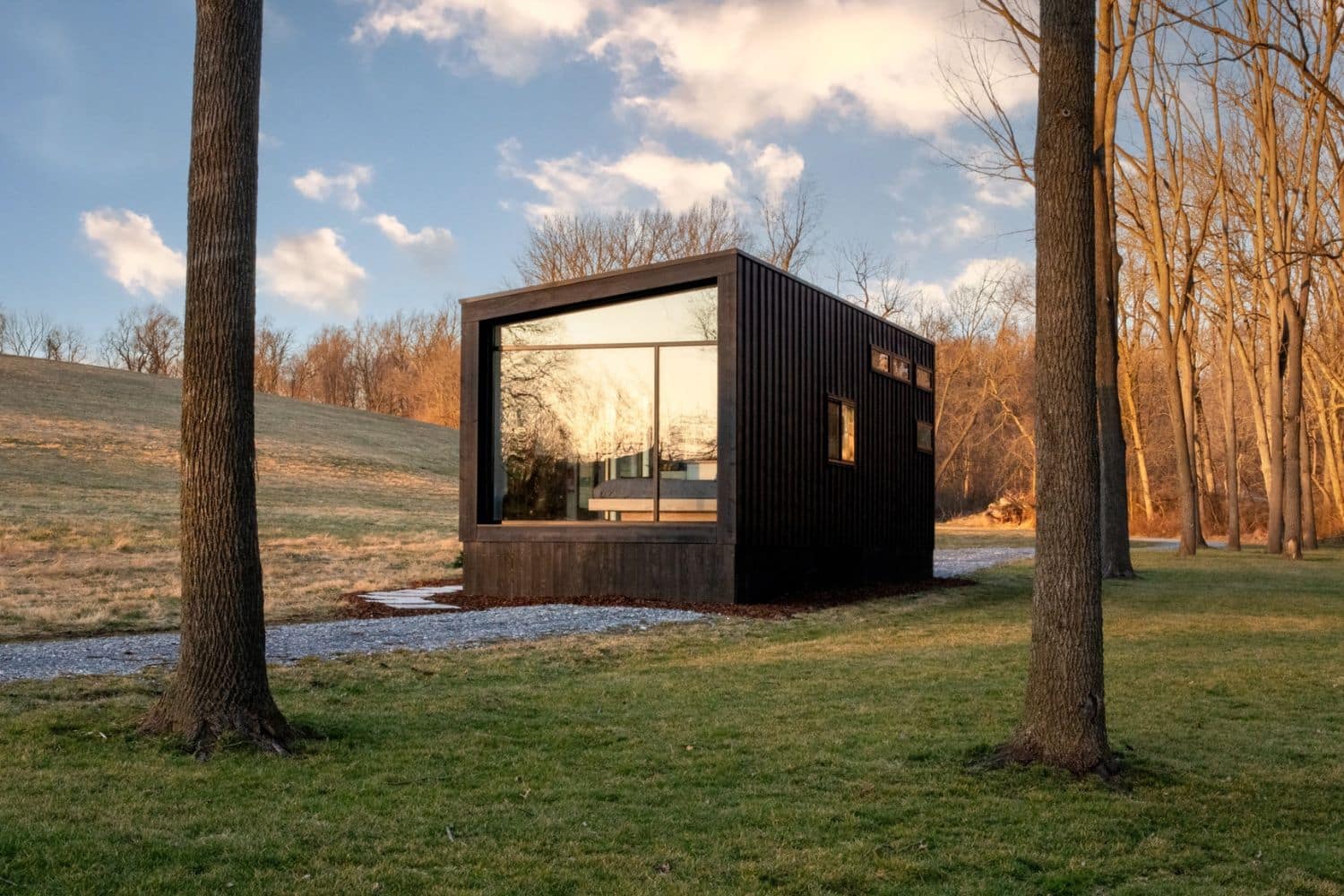 View of side of park model tiny home in clearing with one window on one side between two trees