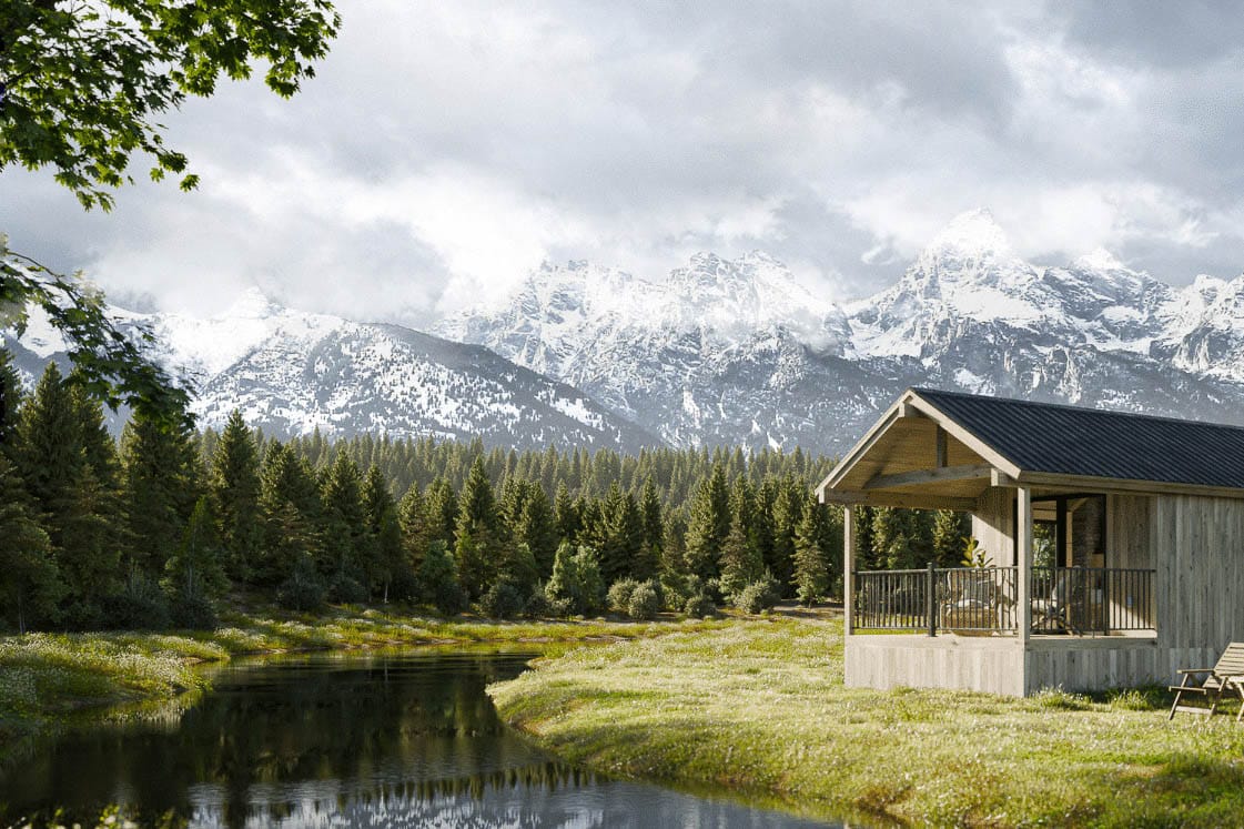 Rustic park model tiny home with wood siding set beside a pond with snow-covered mountains in the background.