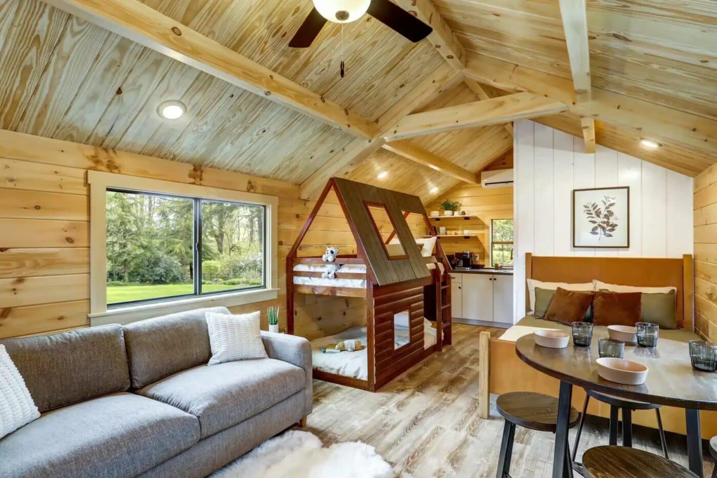 Rustic studio-style park model with exposed wood interior, bunk bed shaped like a log cabin, sofa, and dining table.