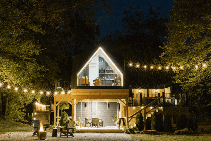a frame park model tiny home raised on platform tree house style with lights on at night