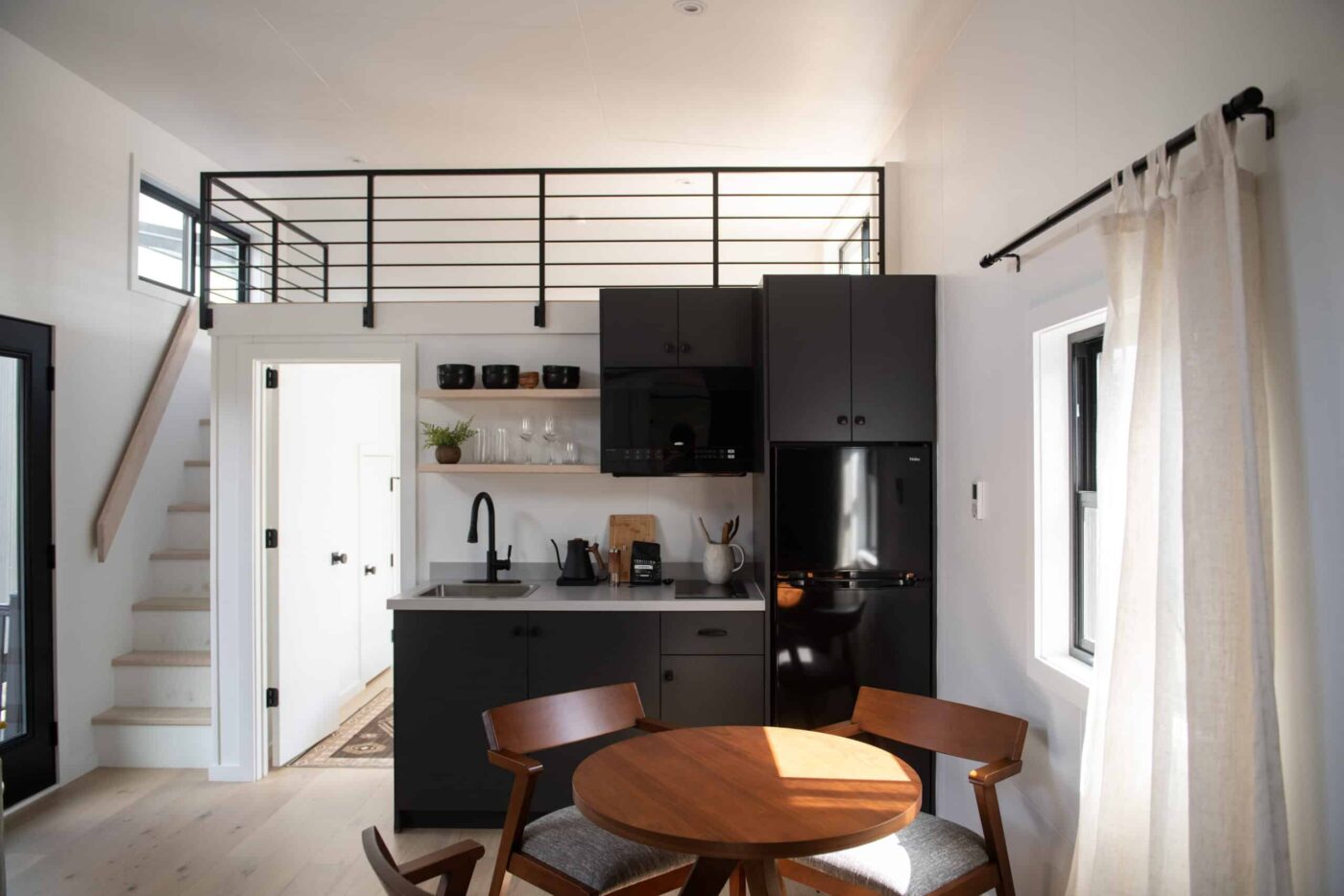 Cascade park model tiny home set near a wooded riverside with outdoor firepit and large windows.