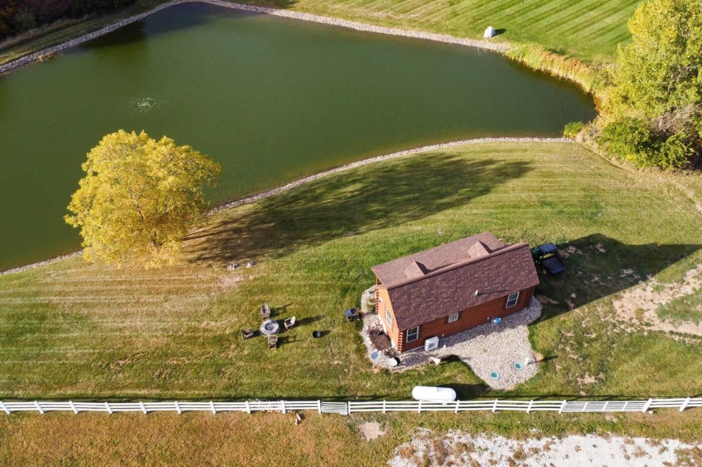 Aerial View of Log Cabin by lake with outdoor seating area, trees, and white fence
