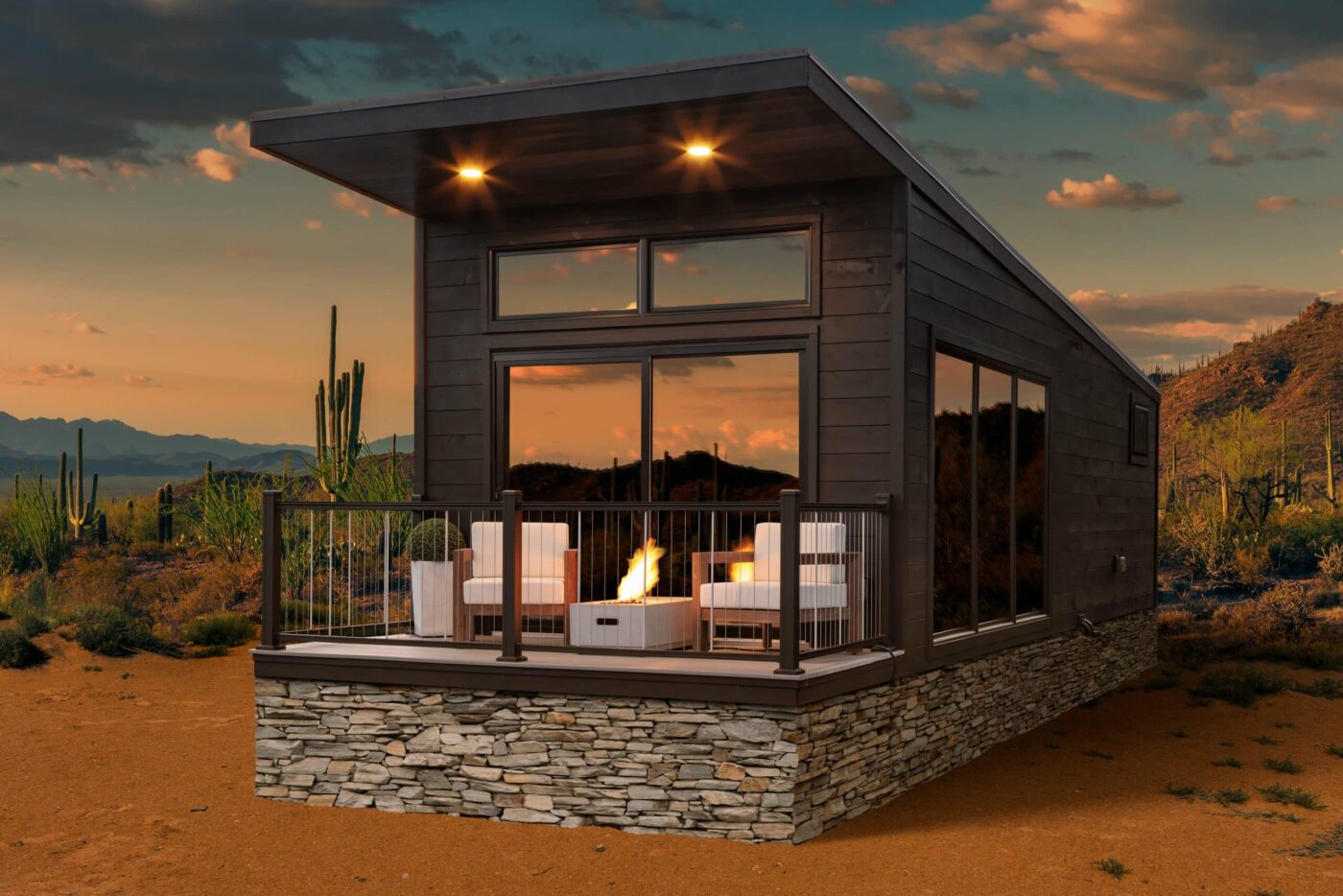 Modern dark exterior park model with large glass windows, stone skirting, and sunset desert backdrop.