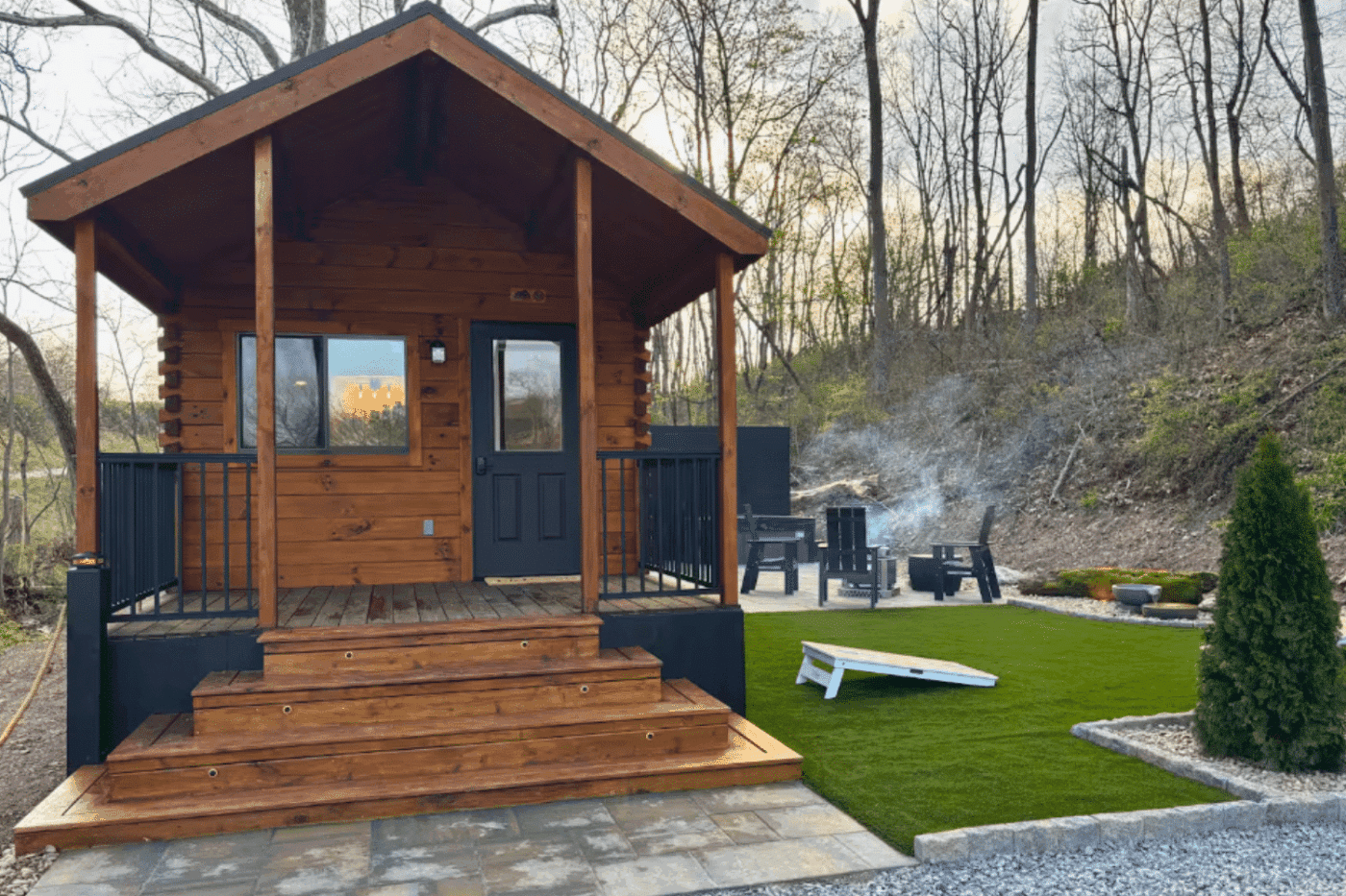 Aspen park model cabin with wood siding, front porch, and outdoor fire pit seating area.