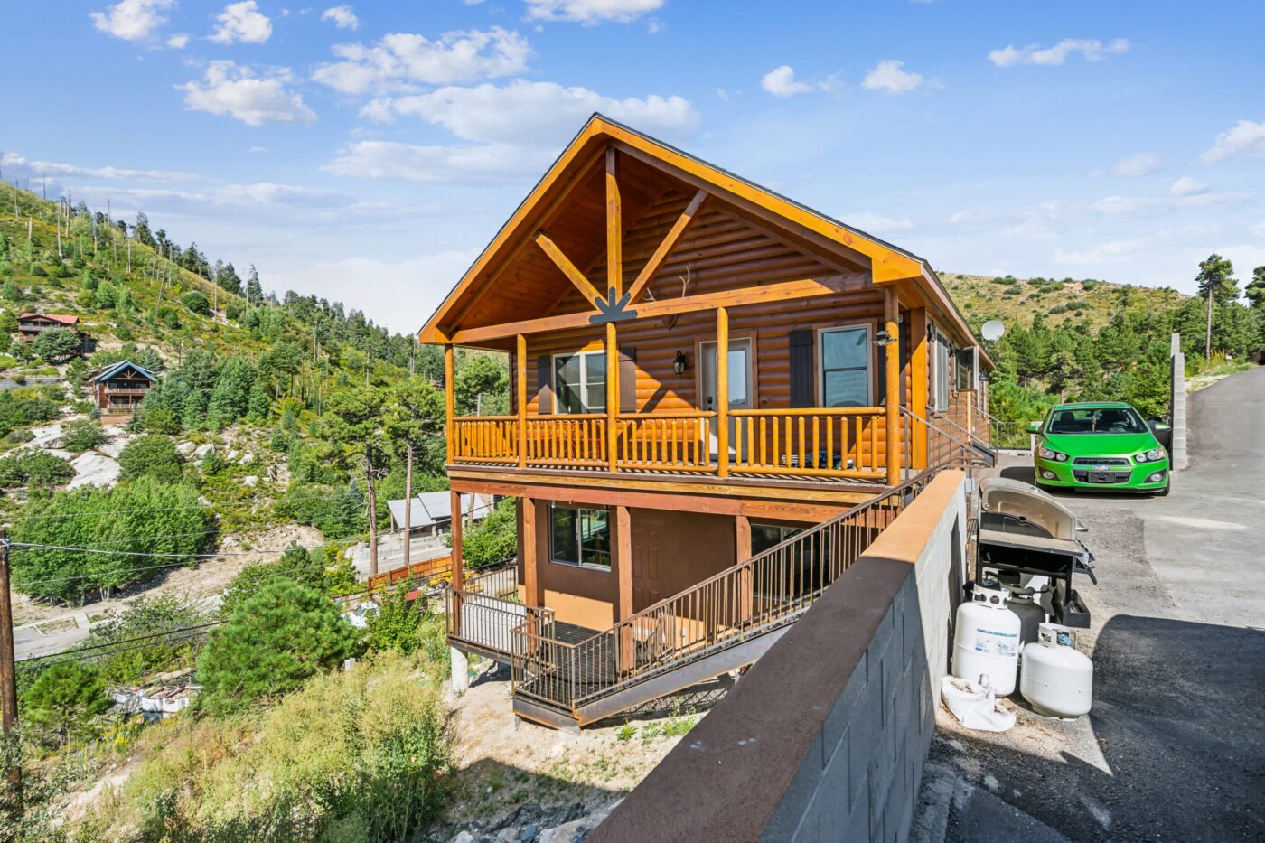 Settler log cabin with a two-story layout, upper deck, and sloped driveway, set in a wooded Idaho hillside.