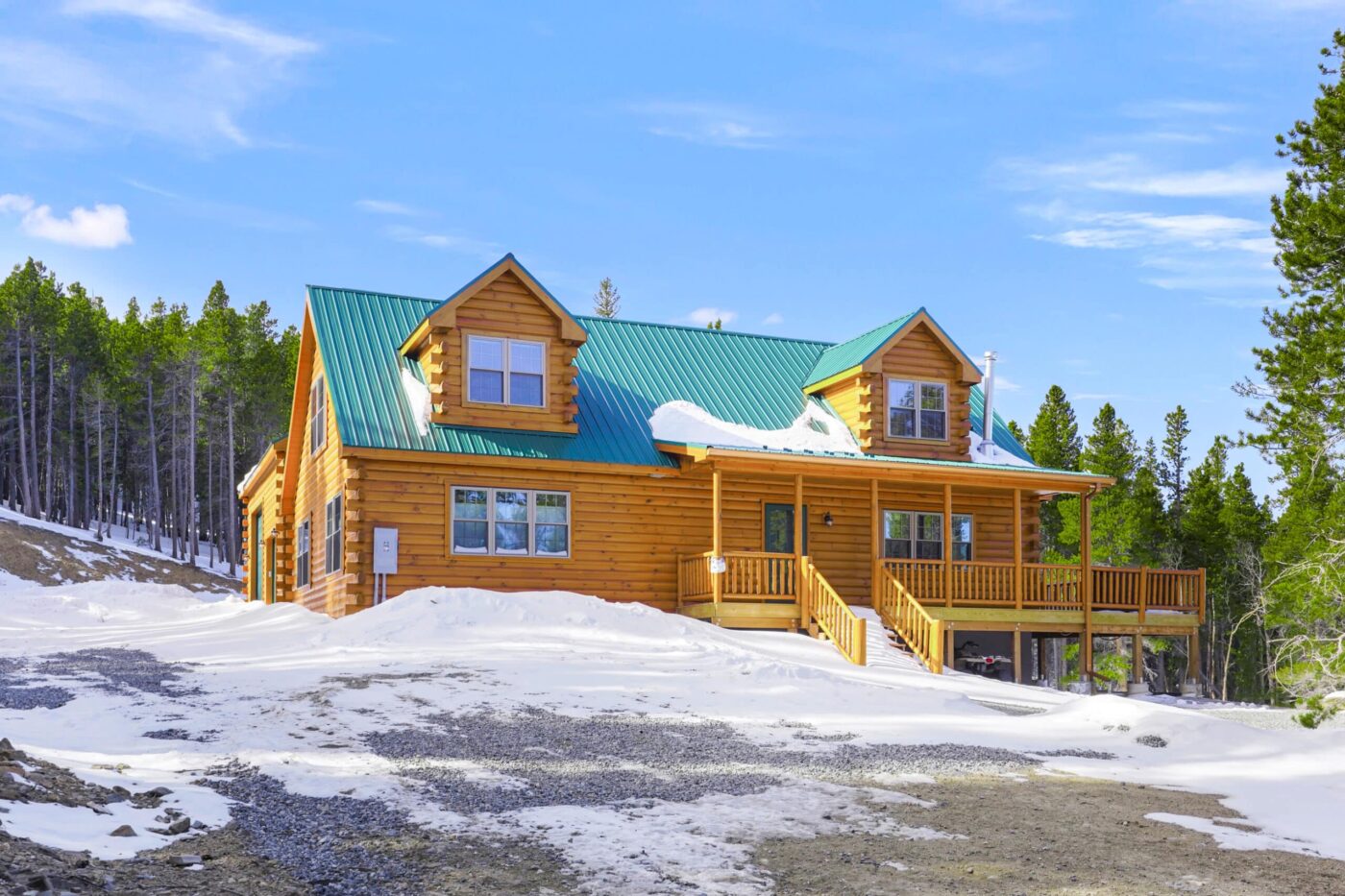 Large two-story log cabin with green metal roof and snow-covered ground.