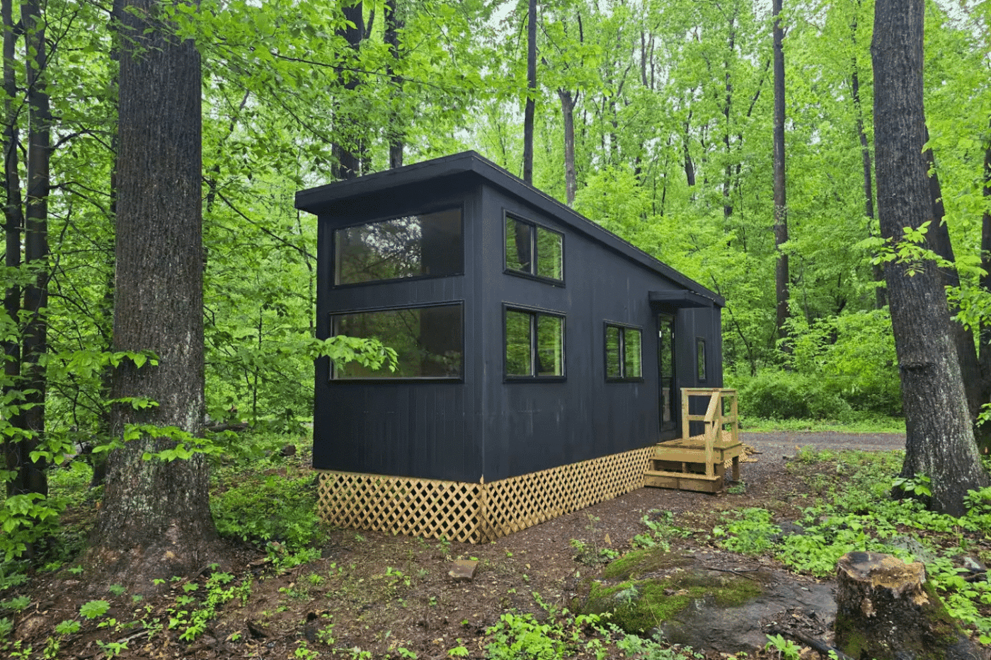 Exterior of Nook Family Park Model tiny home in a wooded setting with black siding and lattice skirting.