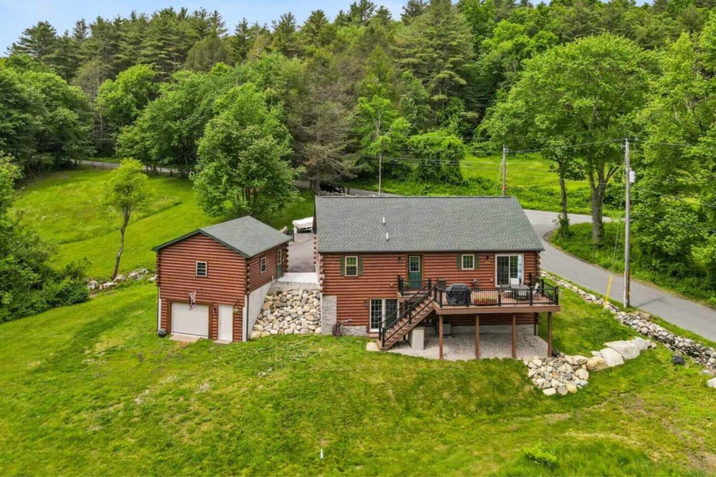 View of log cabin home and log cabin garage from above with view of large back porch and land