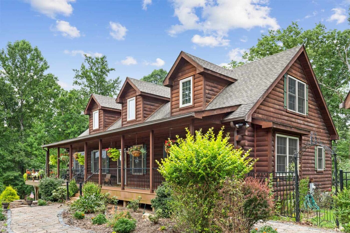 View of dark stained log cabin in garden with iron fence, steps, and porch