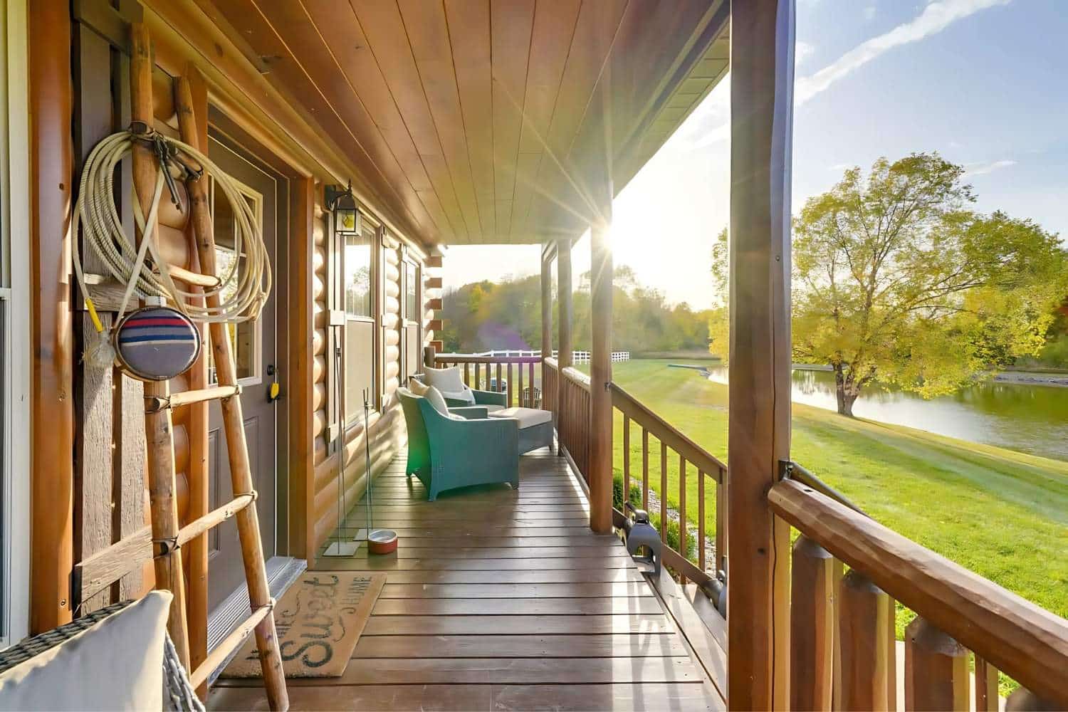 View of log cabin porch next to lake with the sun through the trees
