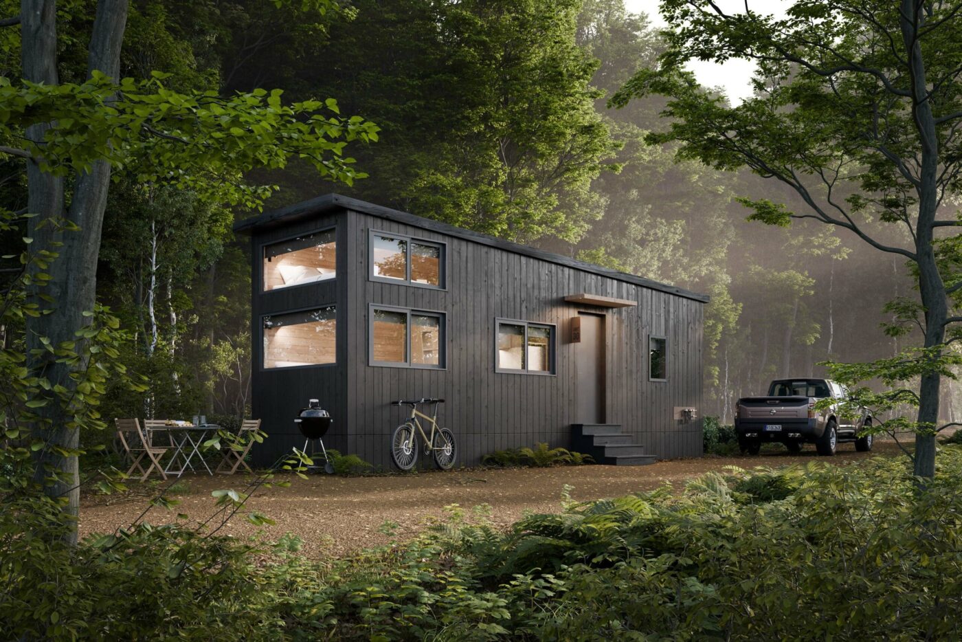 Black modern park model tiny home in a wooded campground, with bicycles, a grill, and a pickup truck parked nearby.