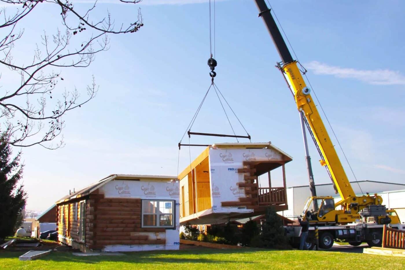 Log Cabin being lowered onto foundation with equipment on sunny day