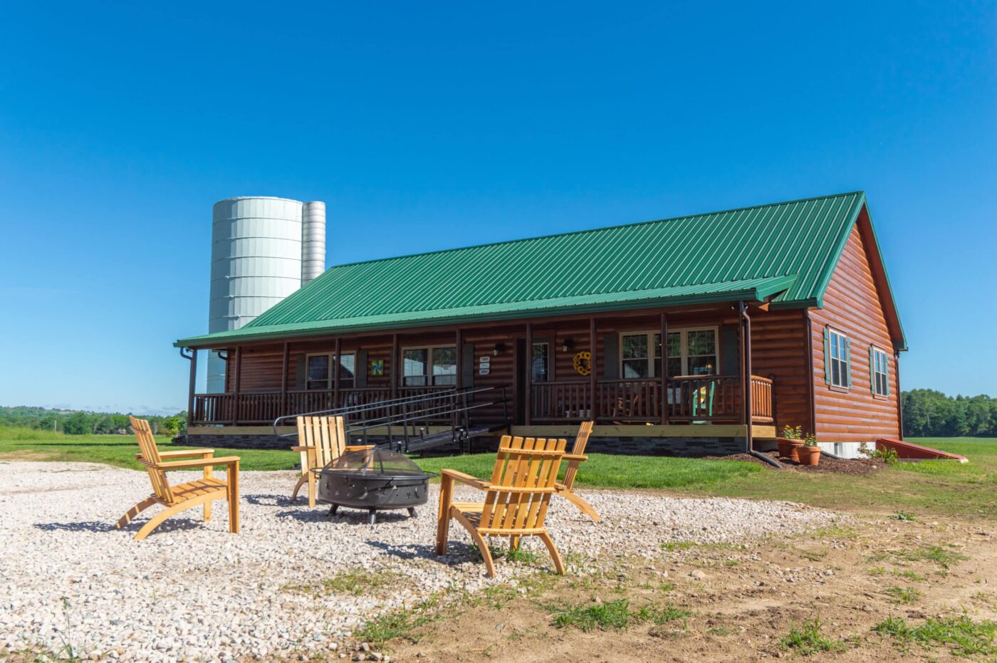 Musketeer log cabin with wide front porch and green roof in a Kentucky setting.