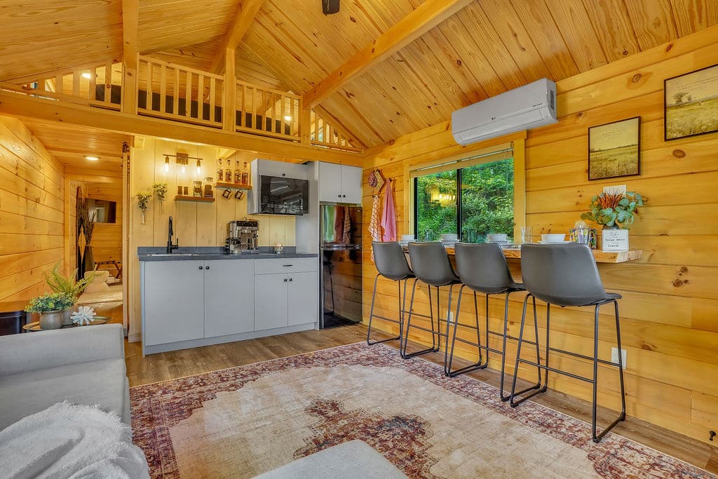 Interior of a log-style Aspen park model with wood-paneled walls, loft, and kitchen featuring bar seating for four.