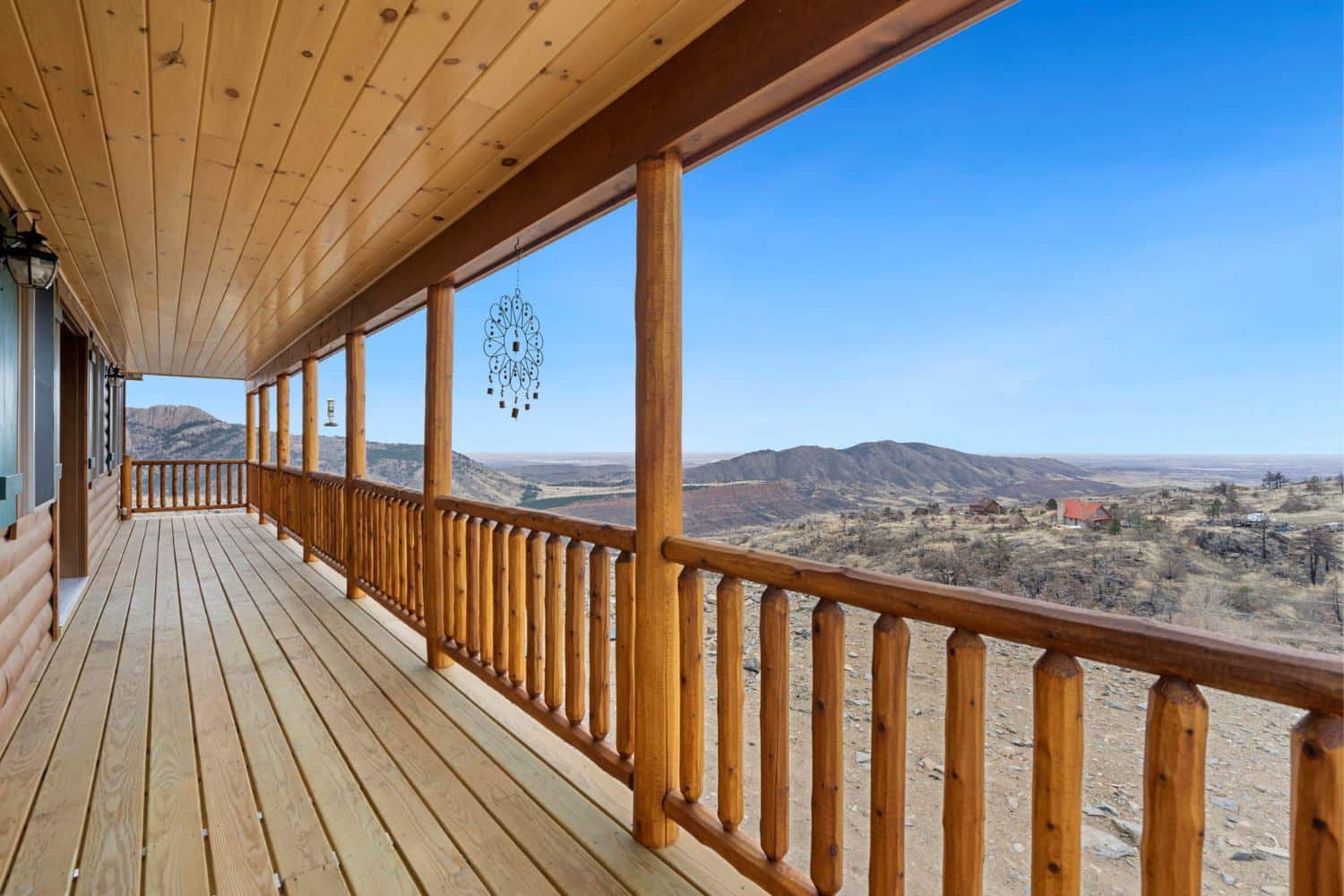View of log cabin porch overlooking mountain canyon. Wind chimes and bird feeder in view